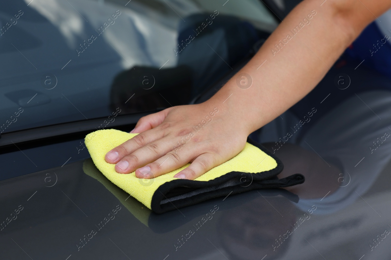 Photo of Man wiping car hood with yellow rag, closeup