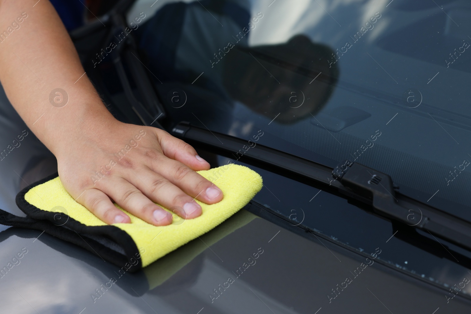 Photo of Man wiping car hood with yellow rag, closeup