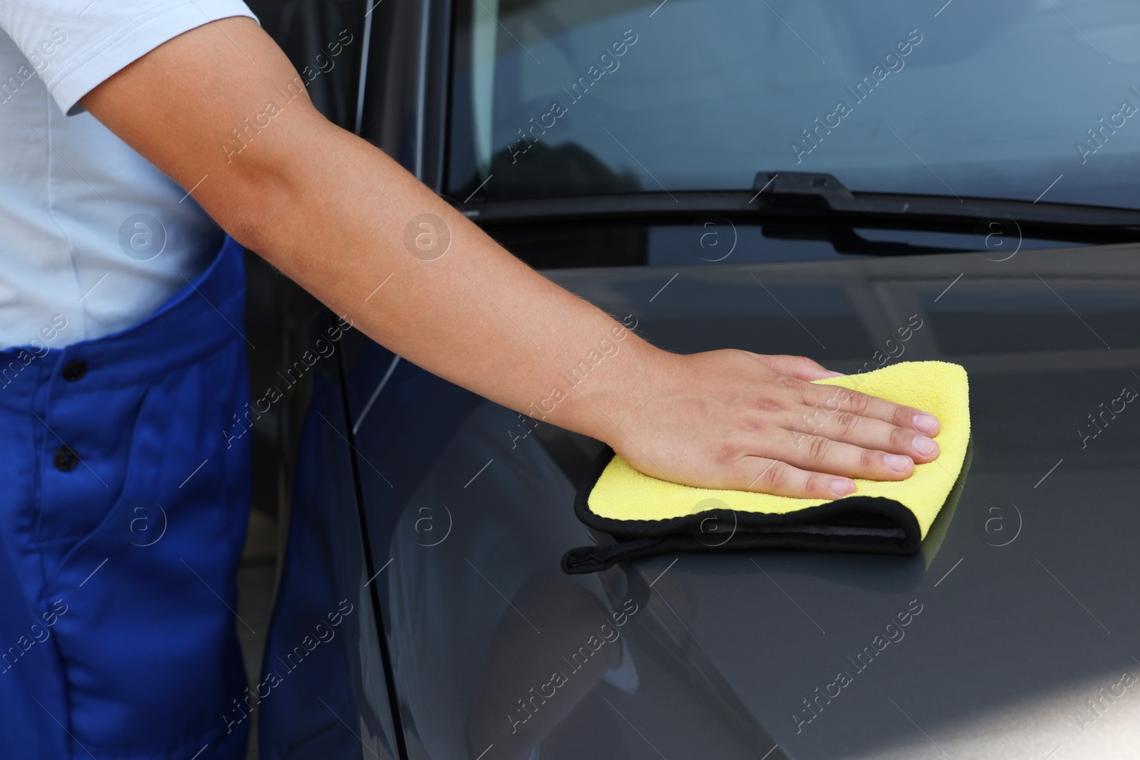 Photo of Man wiping car hood with yellow rag, closeup