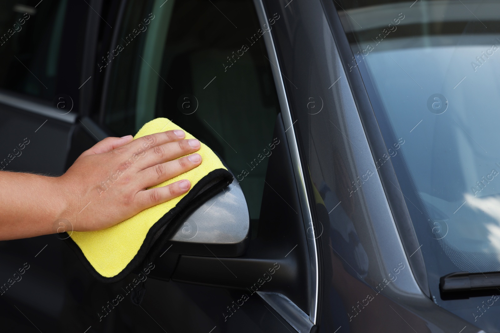 Photo of Man cleaning car side view mirror with yellow rag, closeup