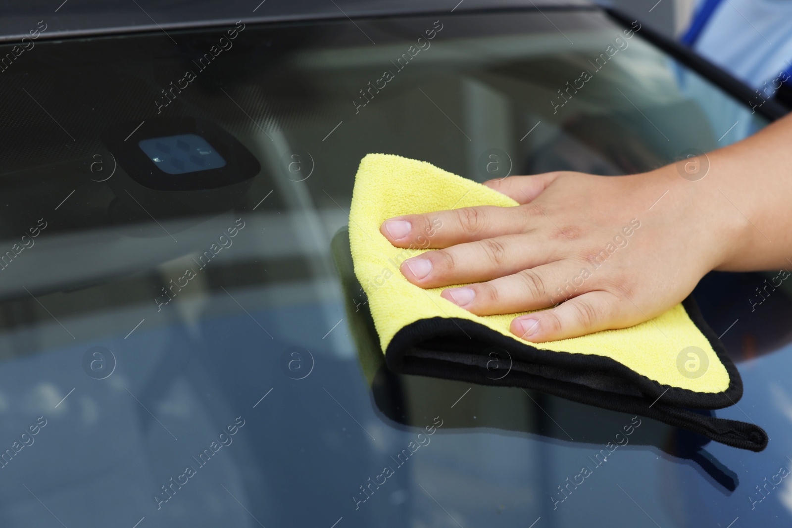 Photo of Man cleaning car windshield with yellow rag, closeup