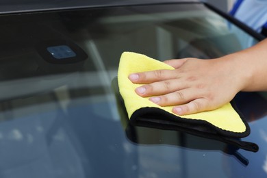 Man cleaning car windshield with yellow rag, closeup