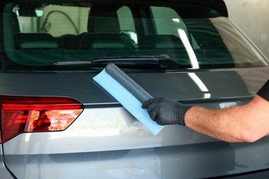 Man wiping auto with squeegee brush at car wash, closeup