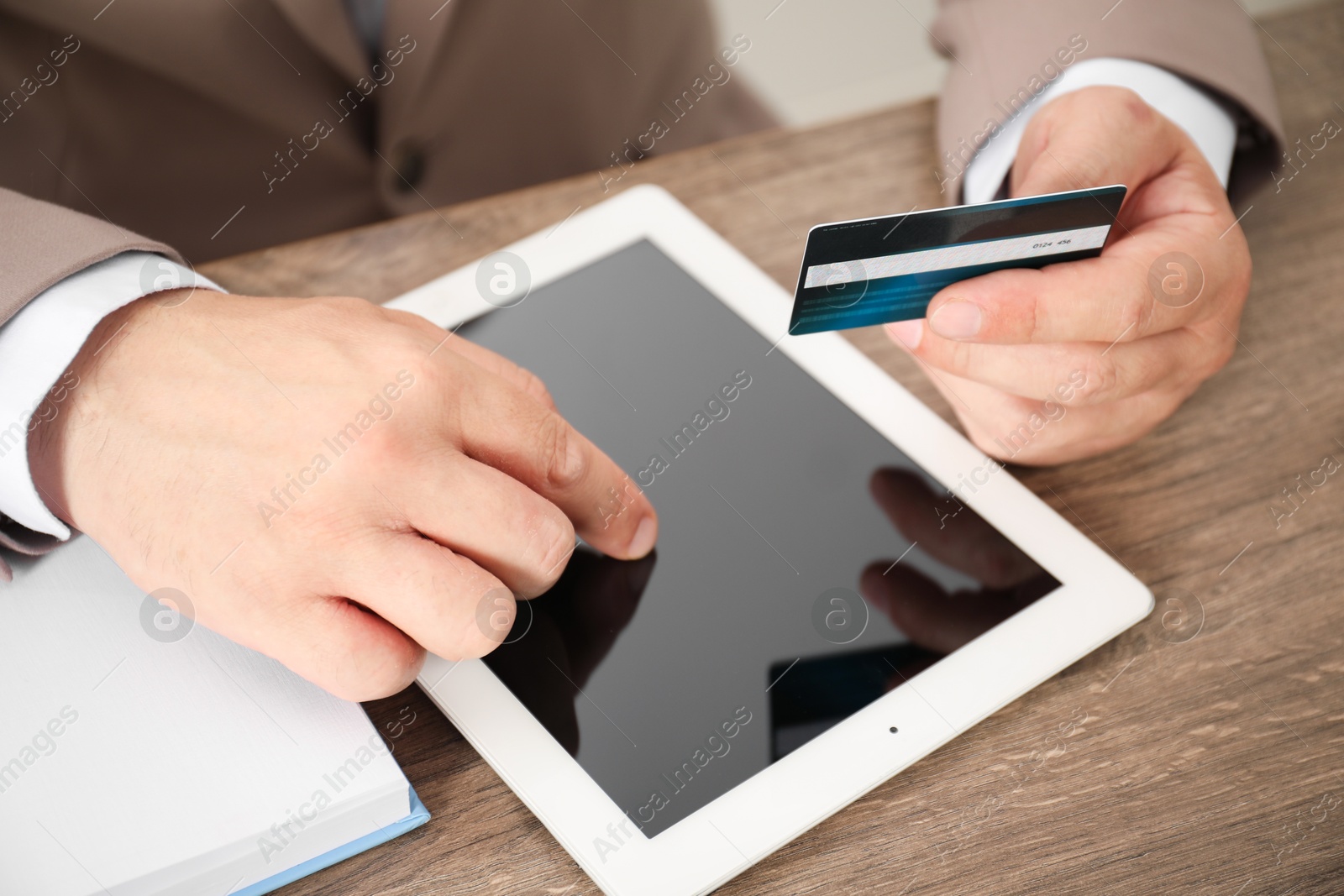 Photo of Man with credit card using tablet at wooden table, closeup