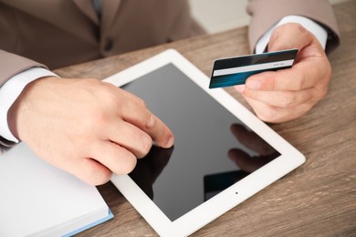 Photo of Man with credit card using tablet at wooden table, closeup