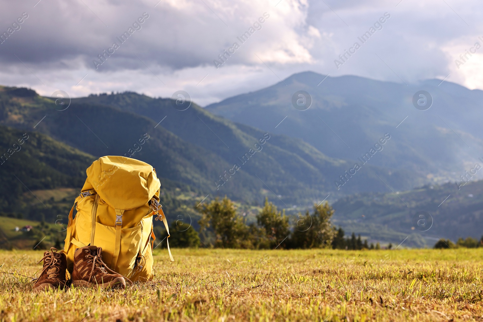 Photo of Backpack and trekking shoes on grass outdoors, space for text