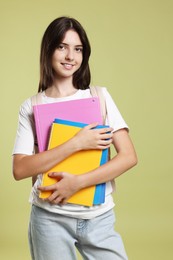 Portrait of cute teenage girl with backpack and books on olive background