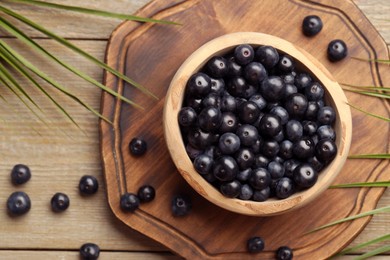 Photo of Ripe acai berries in bowl and palm leaves on wooden table, flat lay