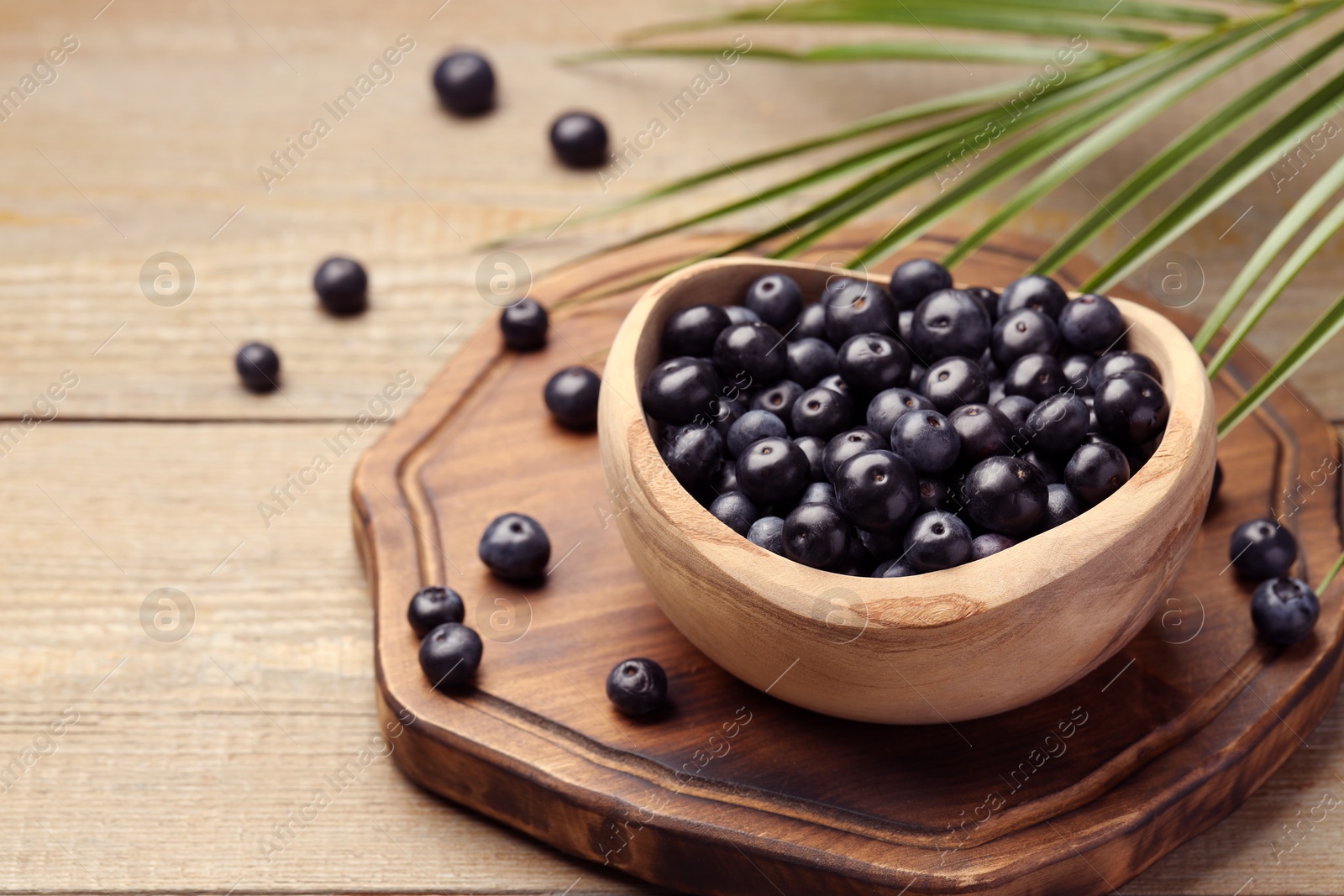 Photo of Ripe acai berries in bowl and palm leaves on wooden table. Space for text