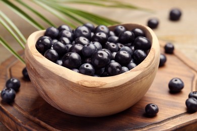 Photo of Ripe acai berries in bowl and palm leaves on wooden table, closeup