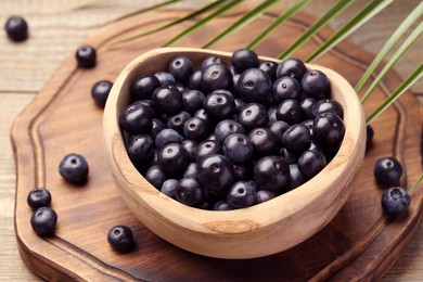 Photo of Ripe acai berries in bowl and palm leaves on wooden table, closeup