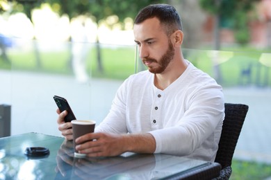 Handsome man using smartphone and drinking coffee at outdoor cafe