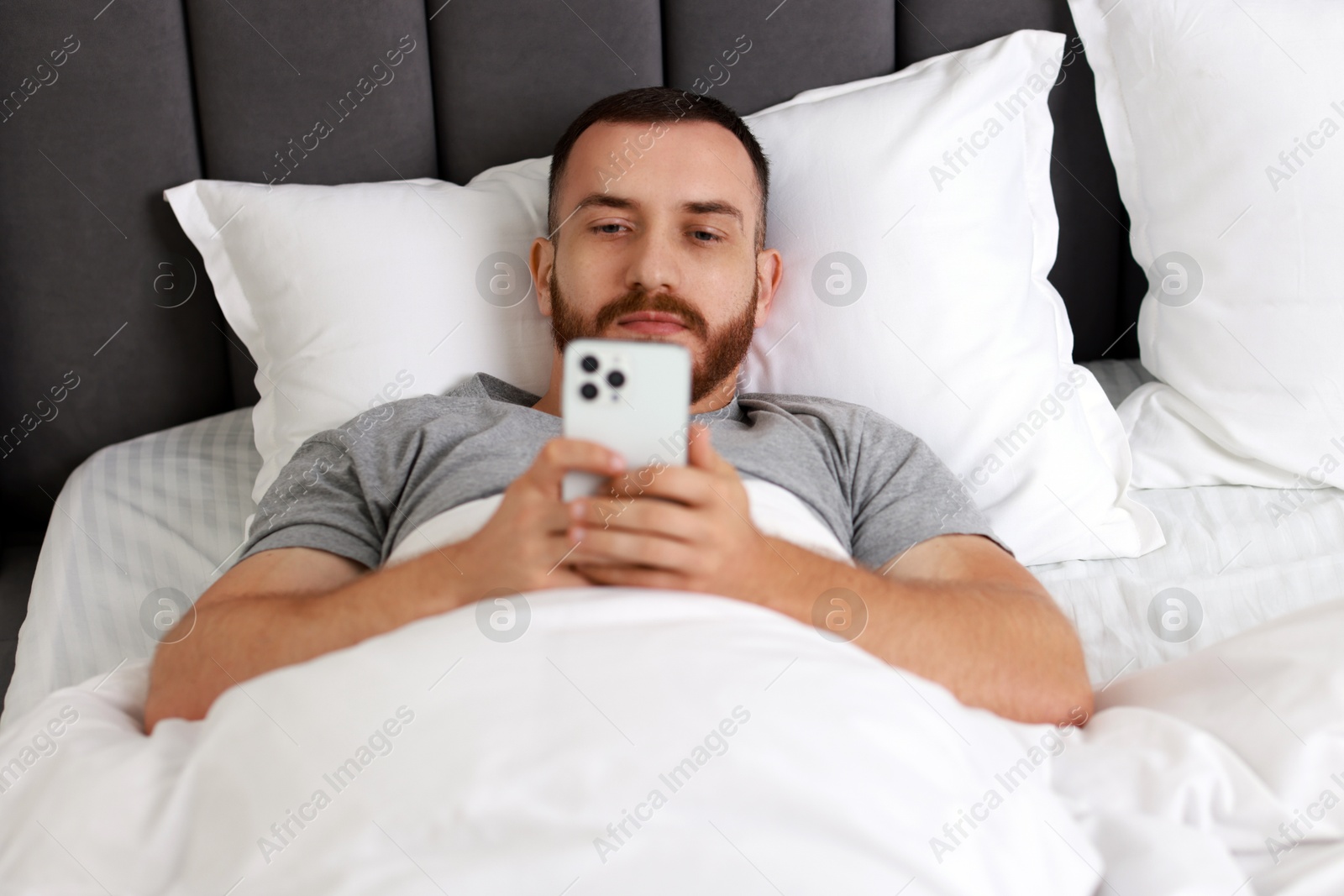 Photo of Handsome man using mobile phone in bed