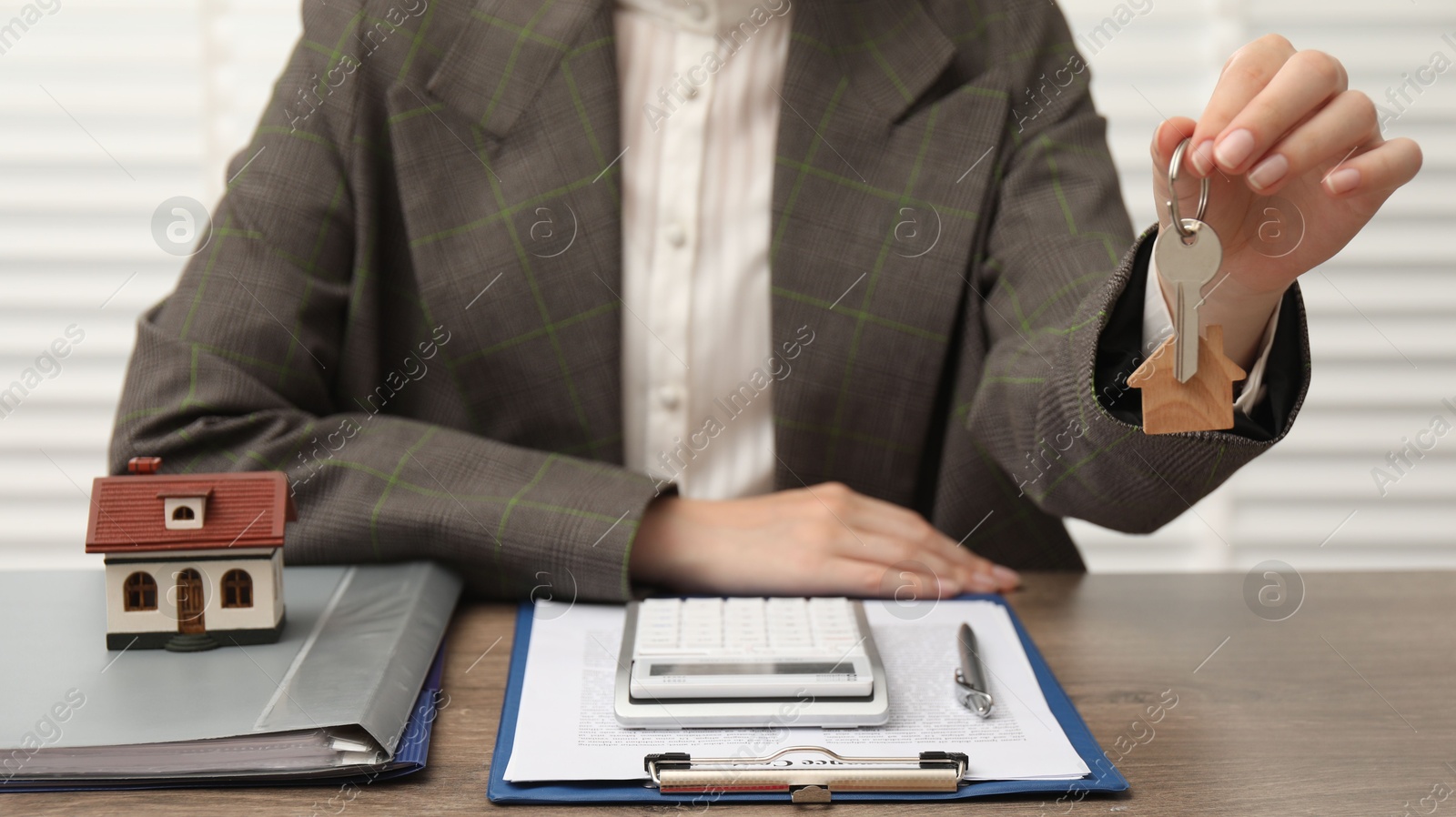 Photo of Real estate agent with house model, key and stationery at wooden table, closeup