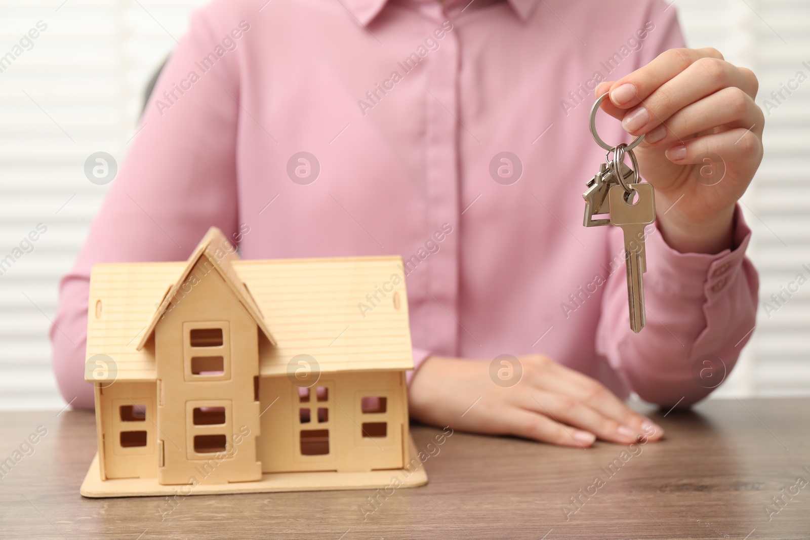 Photo of Real estate agent with house model and key at wooden table, closeup