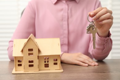 Real estate agent with house model and key at wooden table, closeup