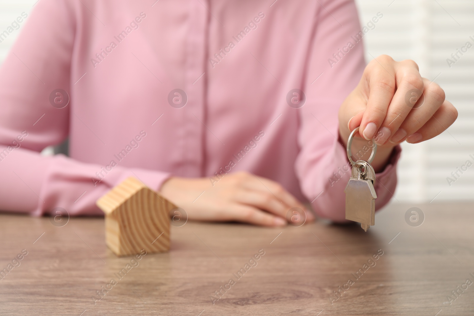 Photo of Real estate agent with house key at wooden table, closeup