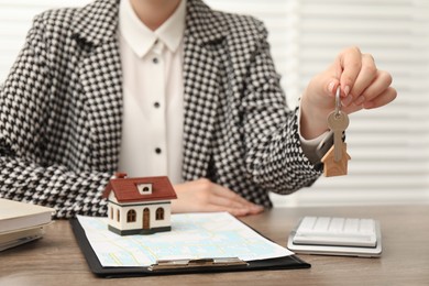 Photo of Real estate agent with house model and key at wooden table, closeup