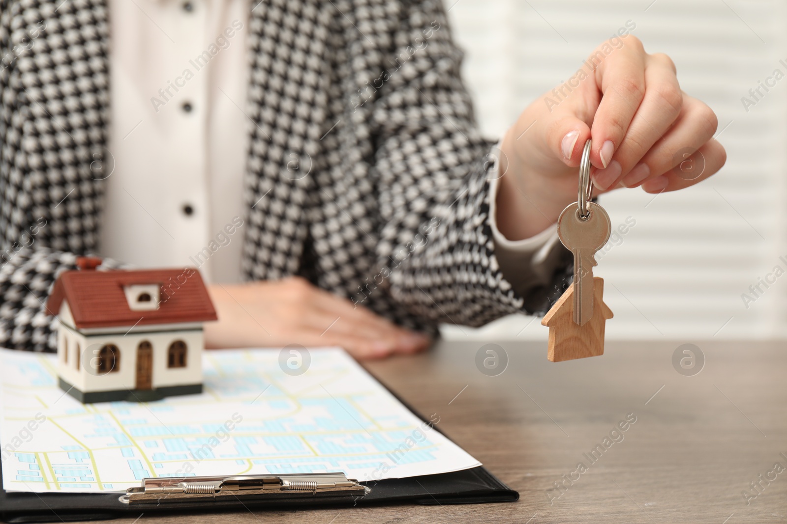 Photo of Real estate agent with house model and key at wooden table, closeup