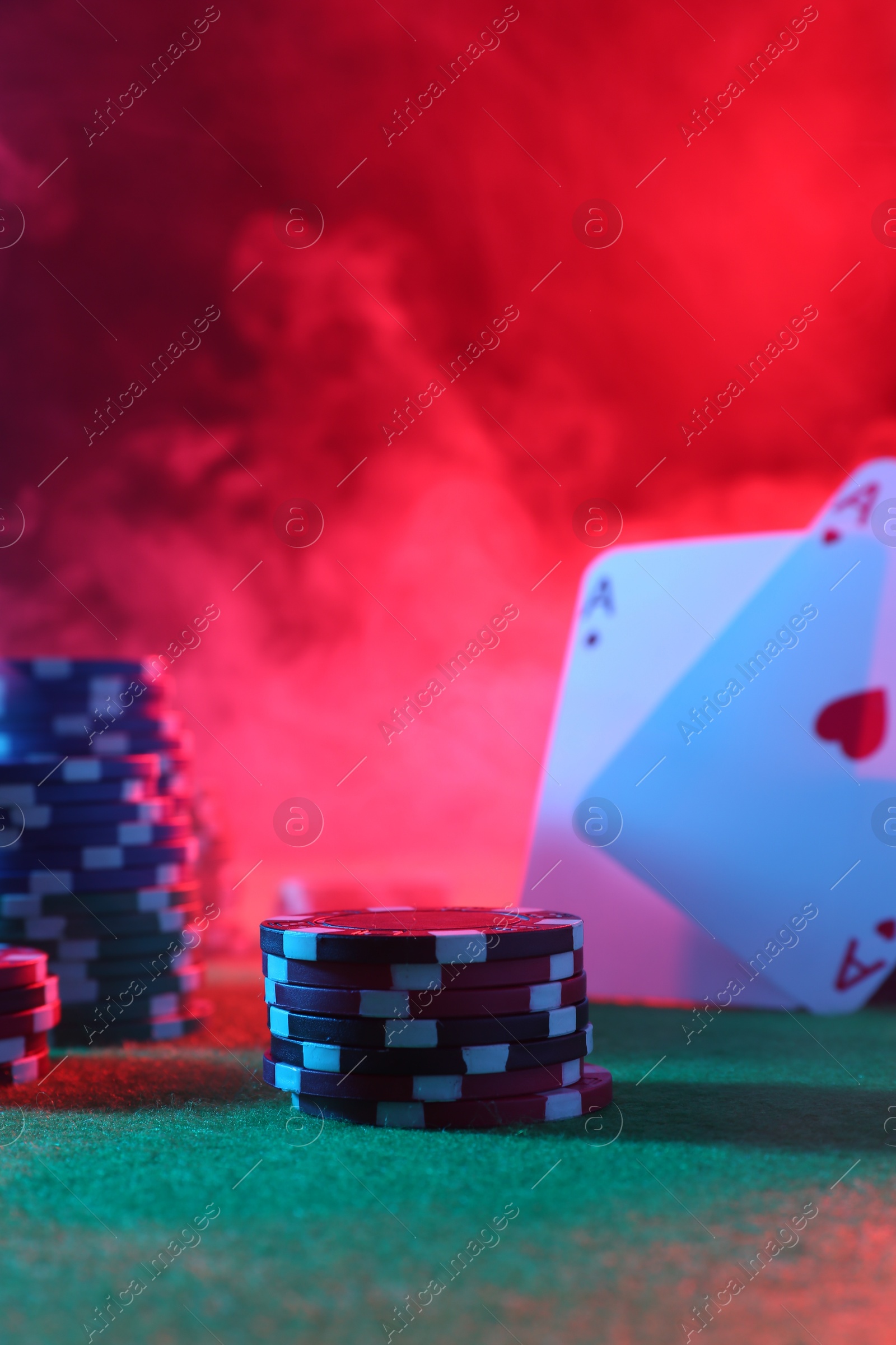 Photo of Poker chips and playing cards on green table in neon lights, closeup