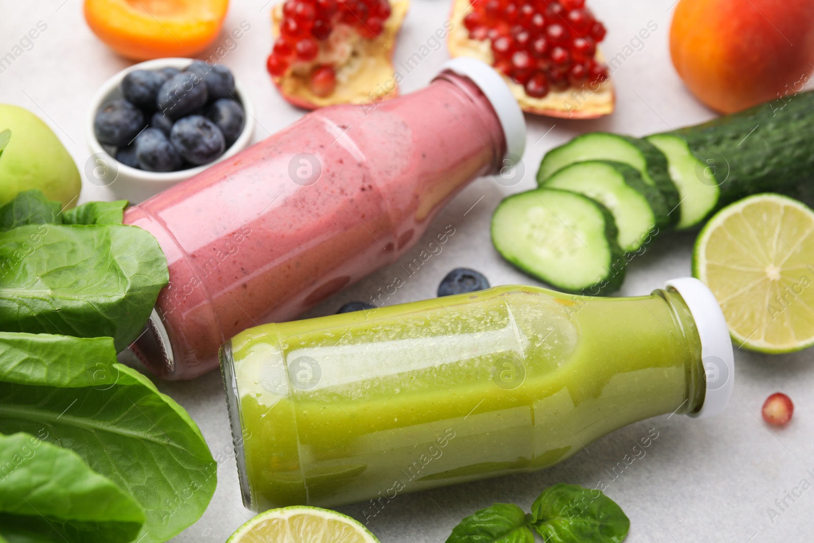 Photo of Glass bottles of tasty smoothies and different products on white table, closeup