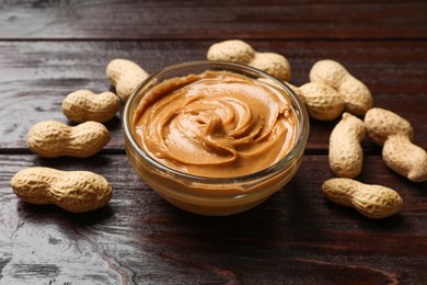 Photo of Tasty peanut butter in bowl and groundnuts on wooden table