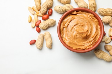 Photo of Tasty peanut butter in bowl and groundnuts on white table, flat lay. Space for text