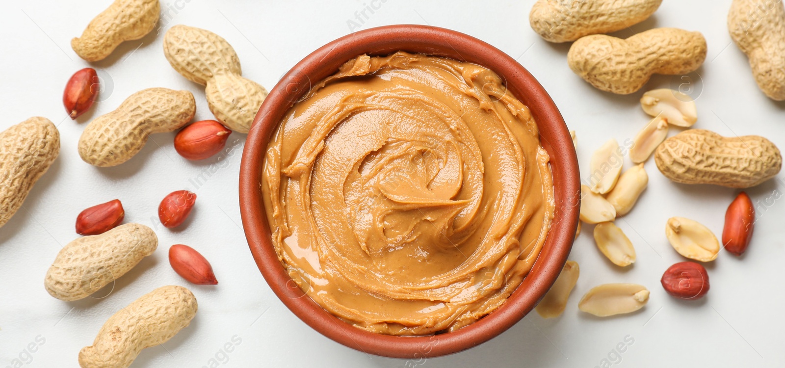 Photo of Tasty peanut butter in bowl and groundnuts on white table, flat lay