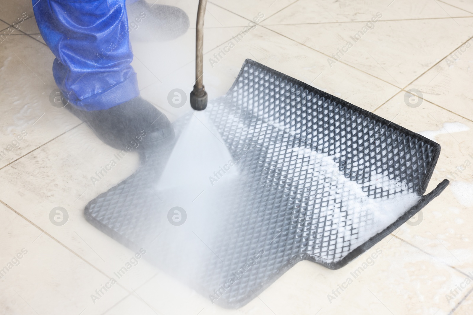 Photo of Man washing rubber car mat with high pressure water jet indoors, closeup