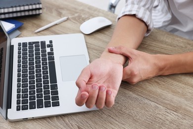 Photo of Man suffering from pain in wrist while working on laptop at table indoors, closeup. Carpal tunnel syndrome