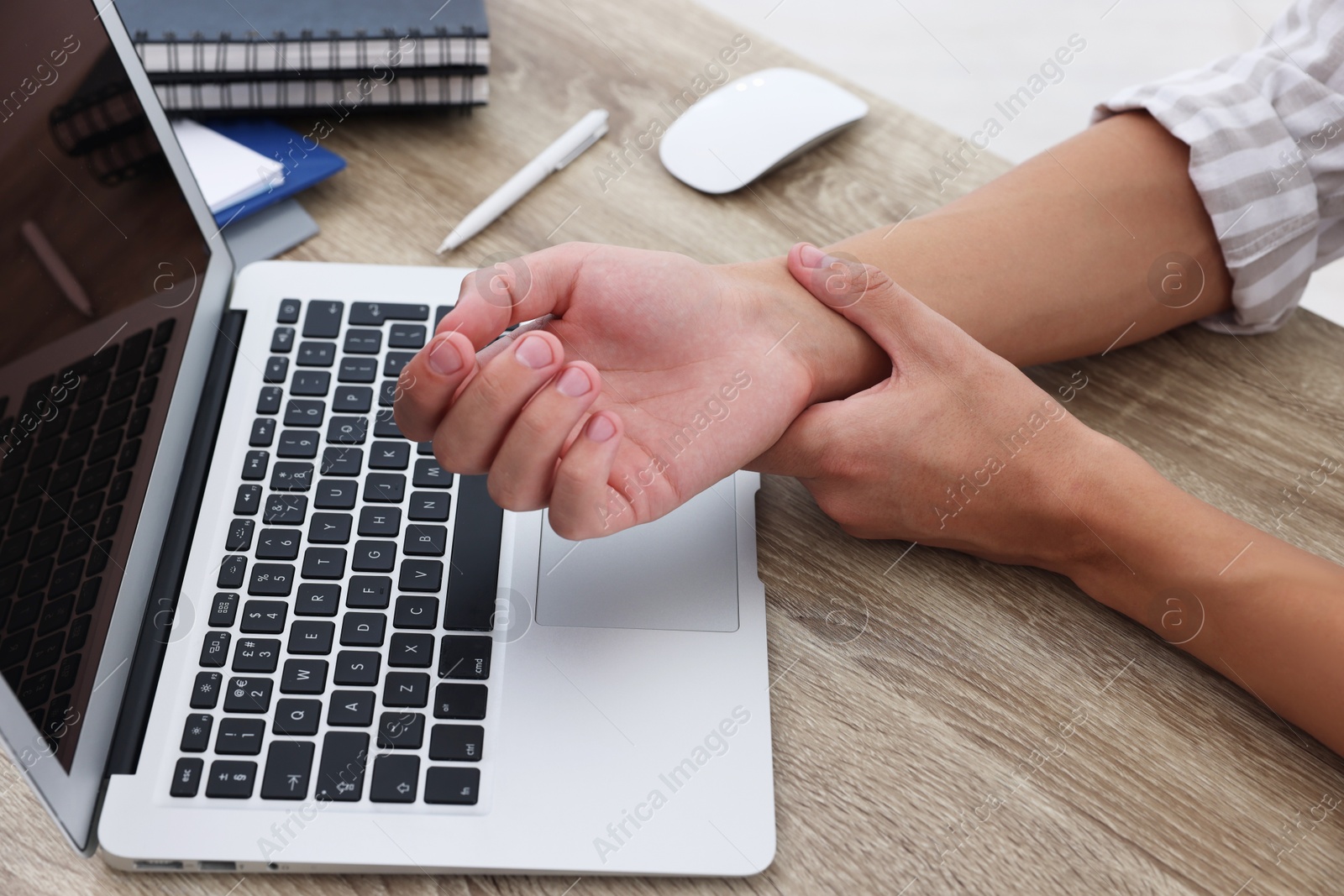 Photo of Man suffering from pain in wrist while working on laptop at table indoors, closeup. Carpal tunnel syndrome