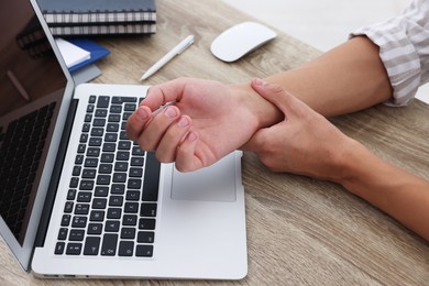 Photo of Man suffering from pain in wrist while working on laptop at table indoors, closeup. Carpal tunnel syndrome