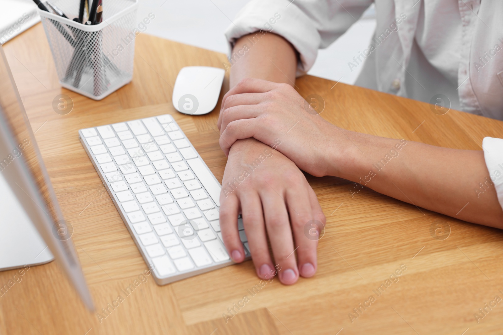 Photo of Man suffering from pain in wrist while working on computer at table indoors, closeup. Carpal tunnel syndrome