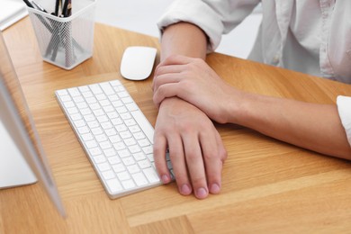 Photo of Man suffering from pain in wrist while working on computer at table indoors, closeup. Carpal tunnel syndrome