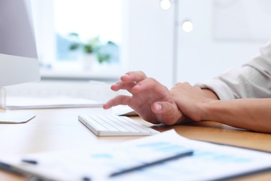 Photo of Man suffering from pain in wrist while working on computer at table indoors, closeup. Carpal tunnel syndrome