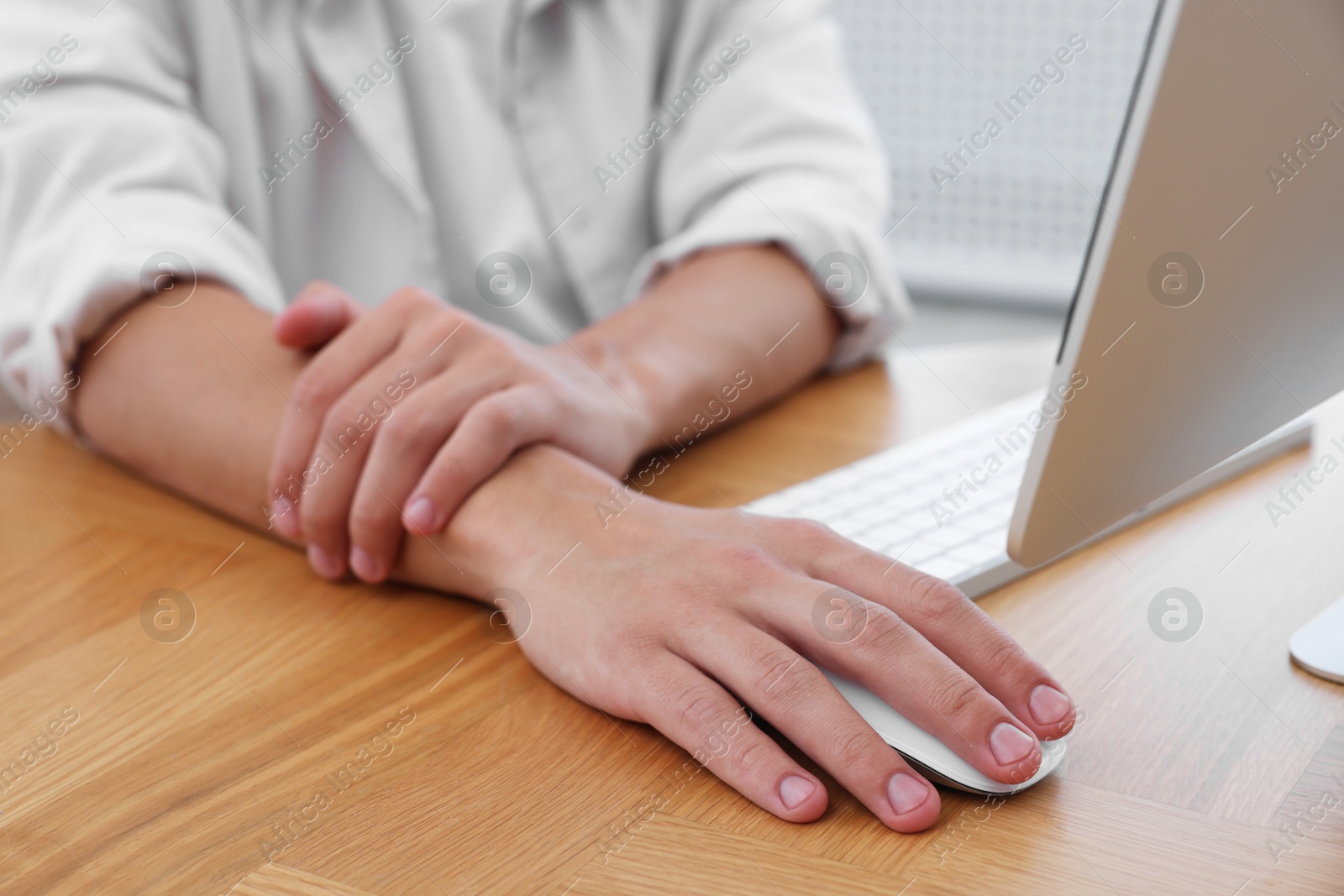 Photo of Man suffering from pain in wrist while working on computer at table indoors, closeup. Carpal tunnel syndrome