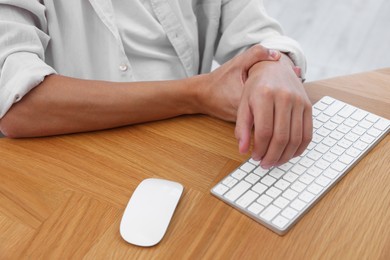 Photo of Man suffering from pain in wrist while working on computer at table indoors, closeup. Carpal tunnel syndrome