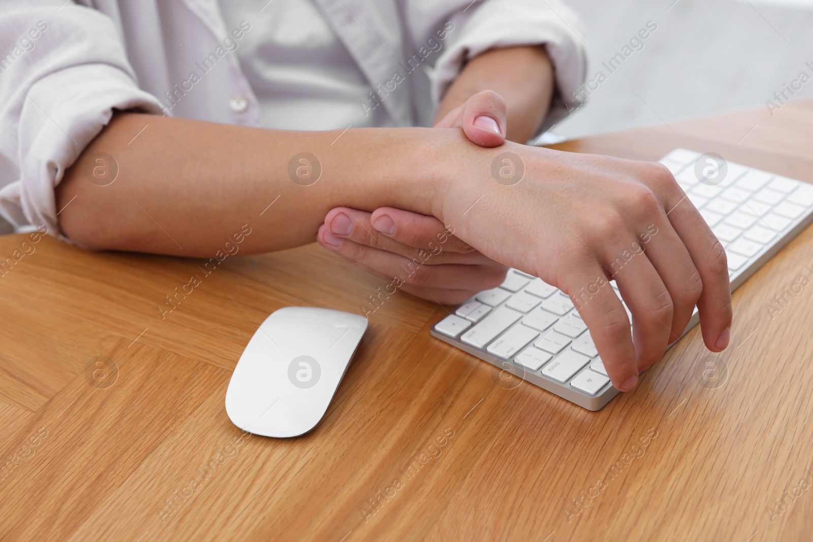 Photo of Man suffering from pain in wrist while working on computer at wooden table, closeup. Carpal tunnel syndrome