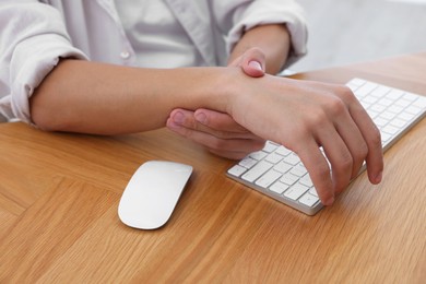 Photo of Man suffering from pain in wrist while working on computer at wooden table, closeup. Carpal tunnel syndrome