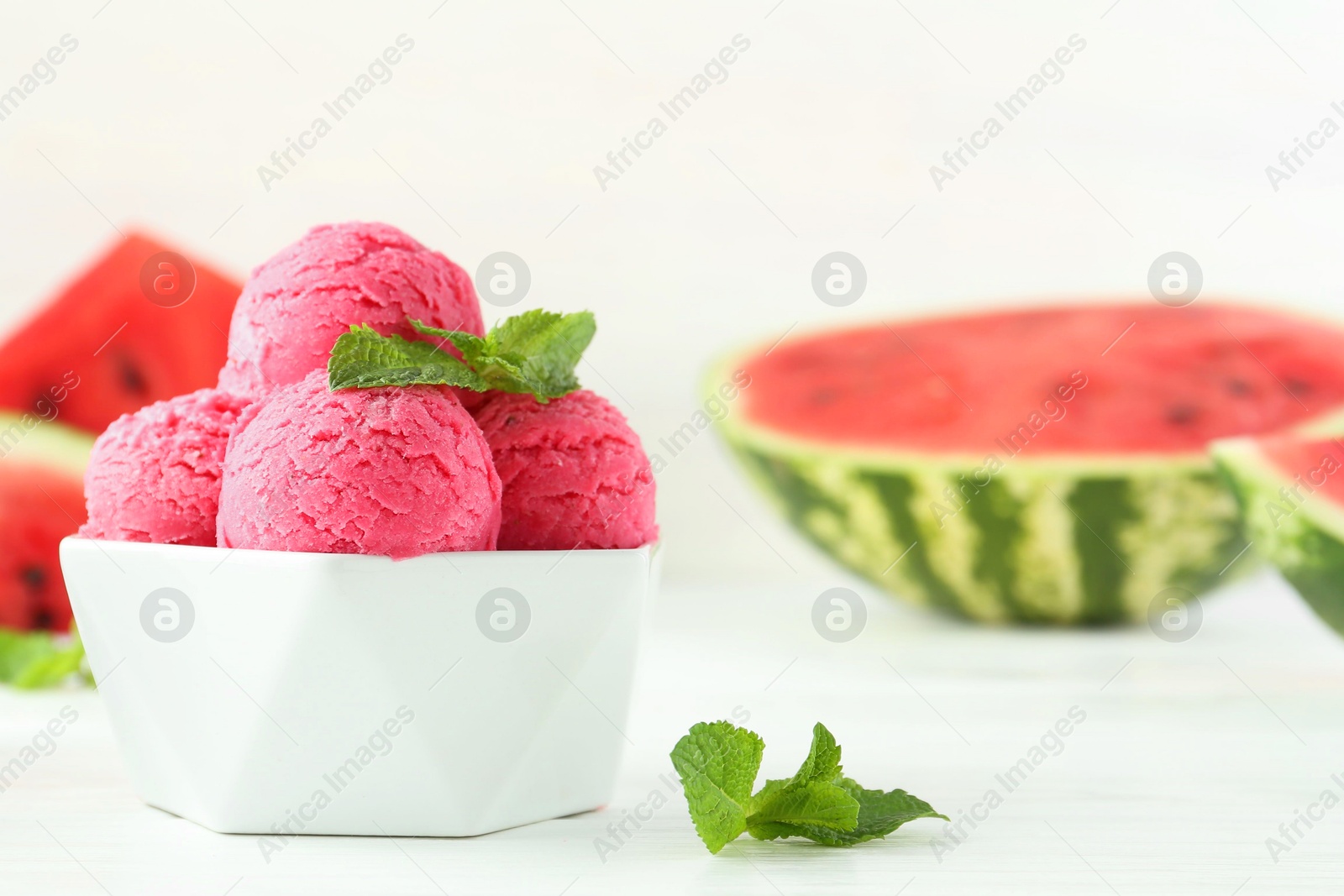 Photo of Scoops of tasty watermelon sorbet with mint in bowl on white table, closeup. Space for text