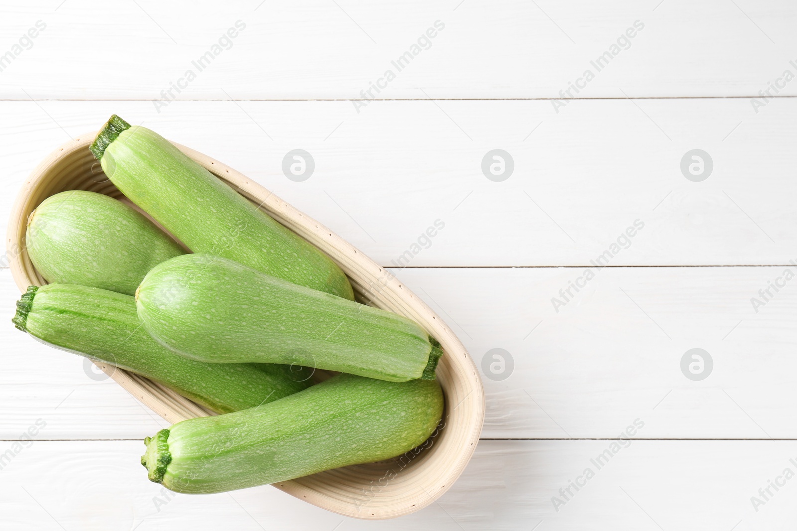 Photo of Fresh zucchinis on white wooden table, top view. Space for text