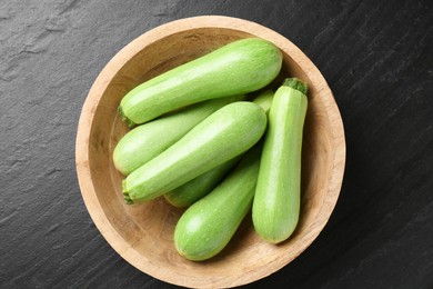 Photo of Fresh zucchinis in bowl on dark textured table, top view