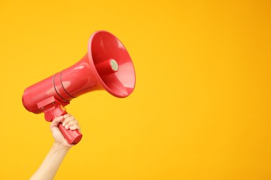 Photo of Woman holding megaphone speaker on orange background, closeup. Space for text