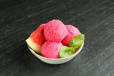 Photo of Scoops of tasty watermelon sorbet with mint and fresh fruit in bowl on grey textured table