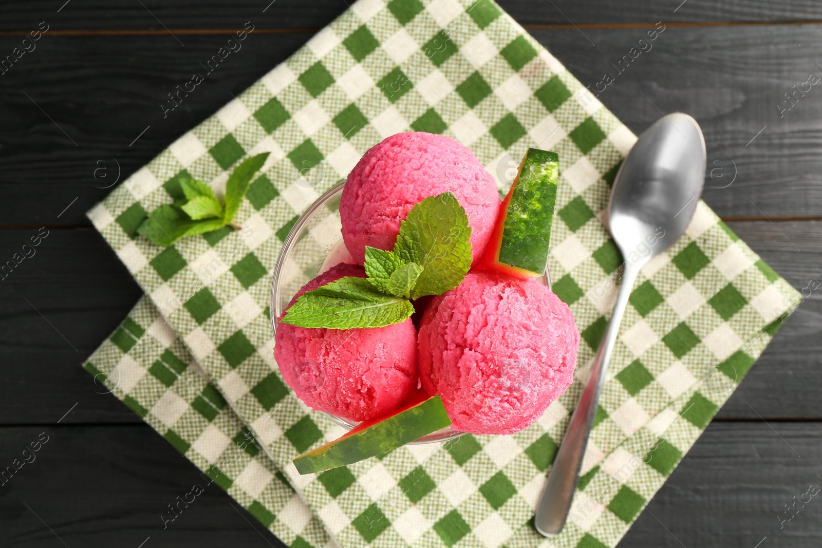 Photo of Scoops of tasty watermelon sorbet in glass dessert bowl with fresh fruit and spoon on black wooden table, flat lay