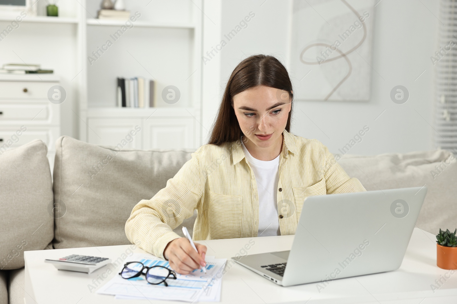 Photo of Budget planning. Young woman with papers using laptop at white table indoors