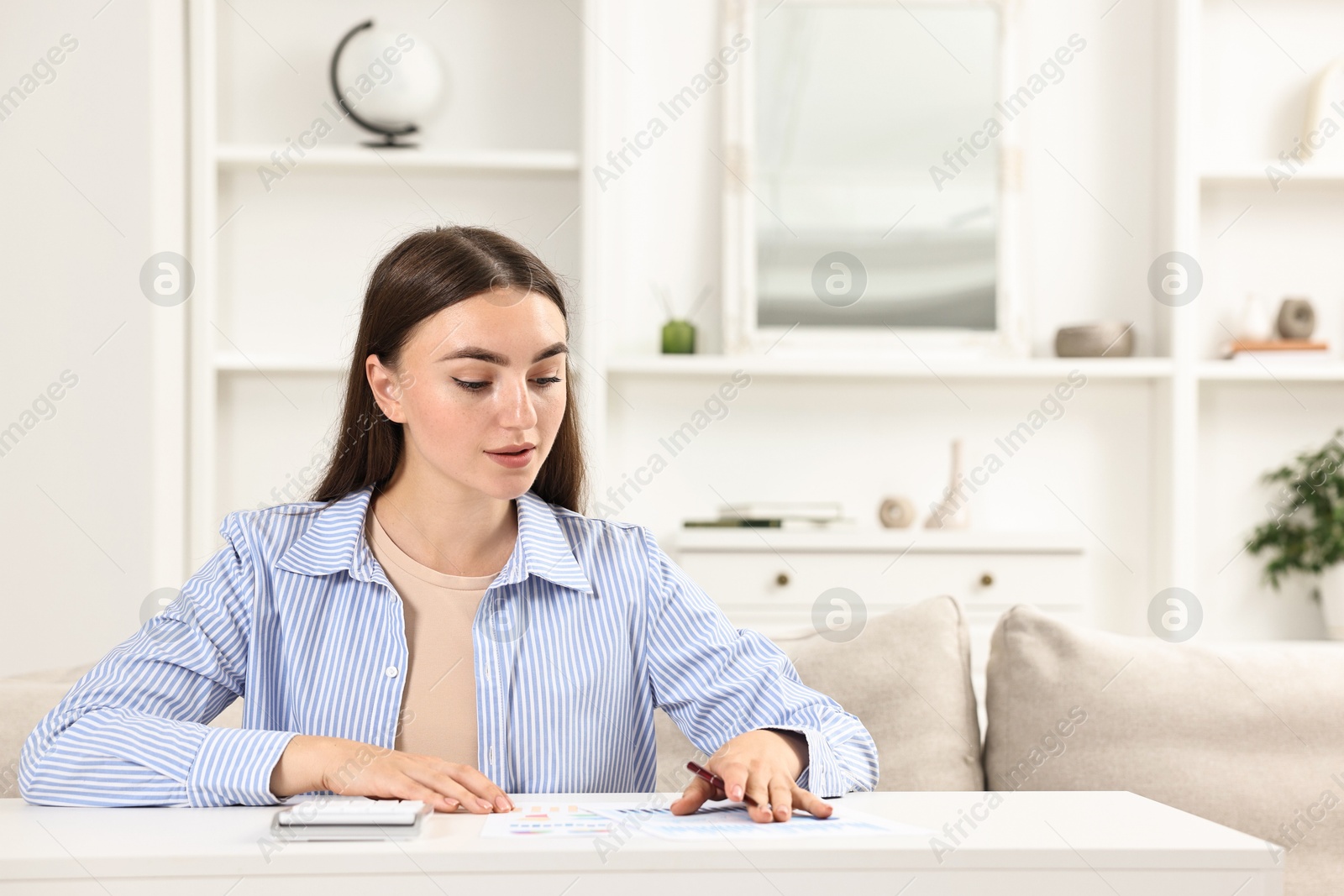 Photo of Budget planning. Beautiful young woman with papers and calculator at white table indoors