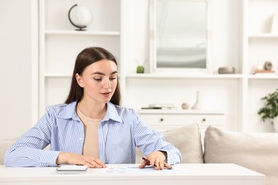 Photo of Budget planning. Beautiful young woman with papers and calculator at white table indoors