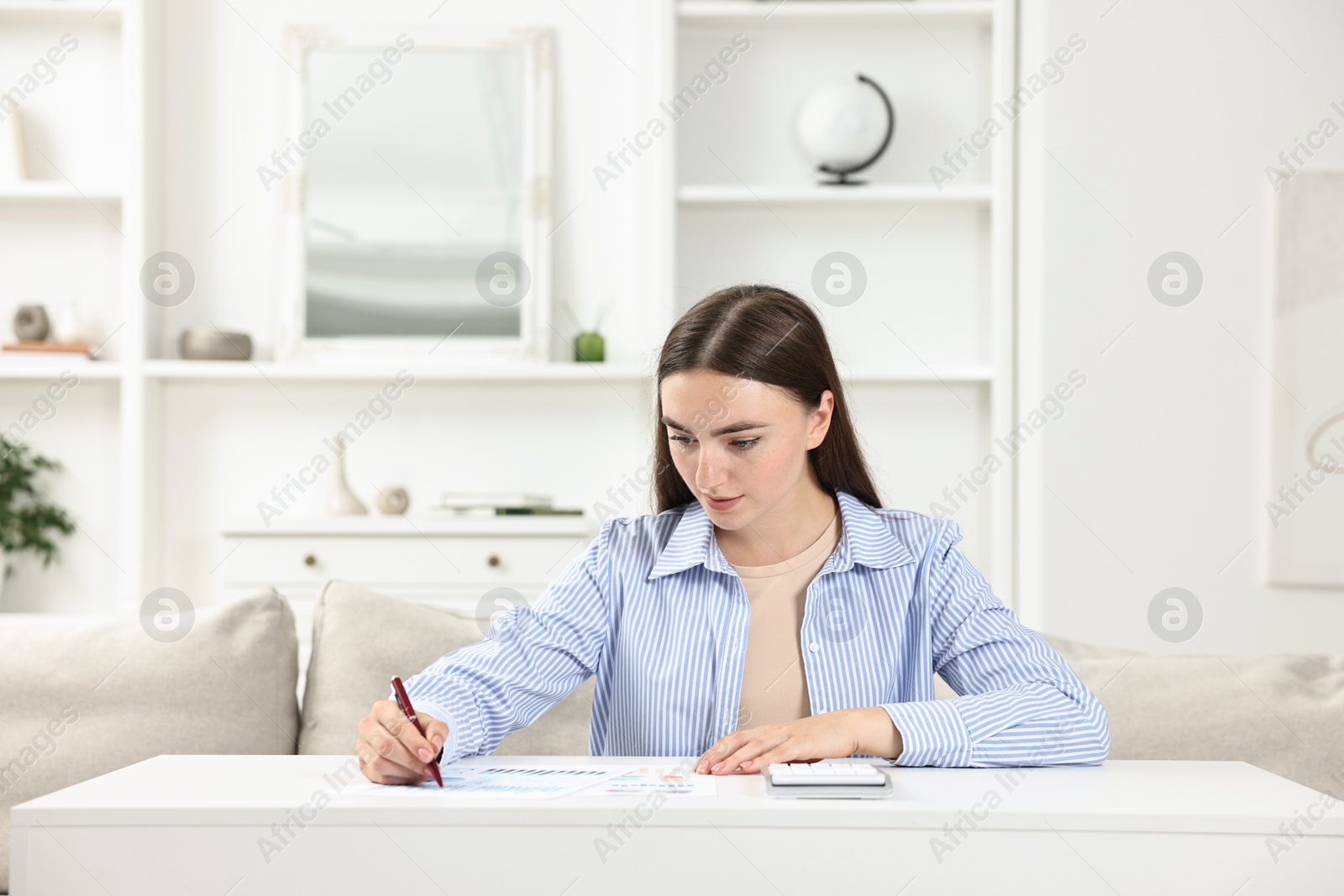 Photo of Budget planning. Beautiful young woman with papers and calculator at white table indoors