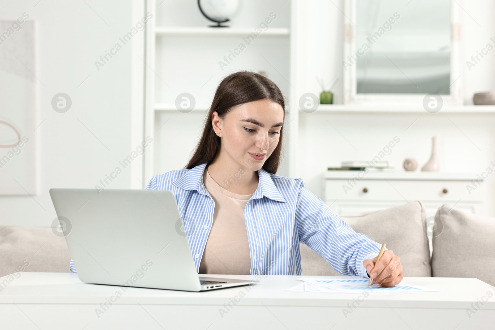 Photo of Budget planning. Beautiful young woman with papers and laptop at white table indoors